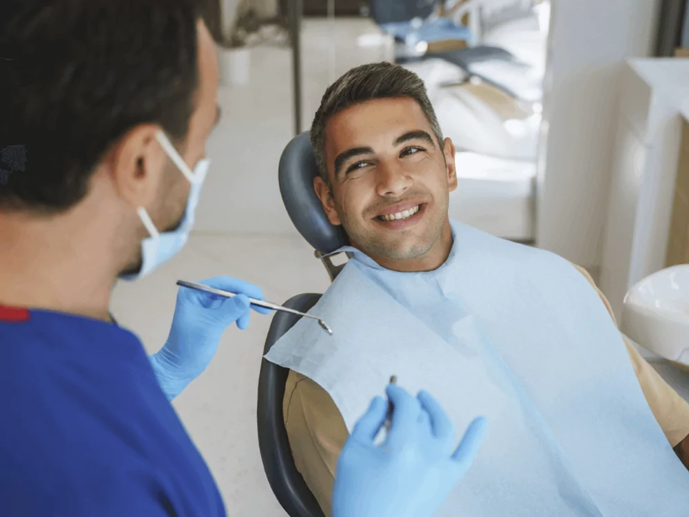 a patient sitting in an operating chair smiling at a dentist holding dental tools